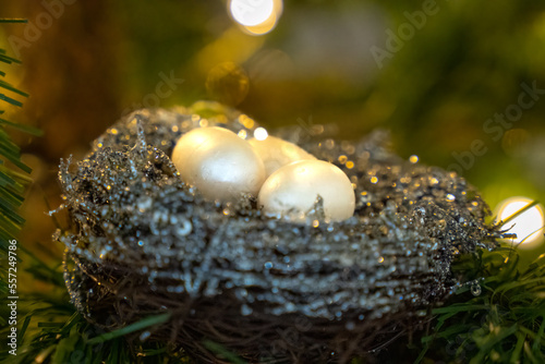 Eggs in a birds nest Christmas ornament in an artificial Christmas tree with Christmas light in background