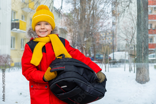 Boy with backpack sits at bus stop and waits for bus in winter.