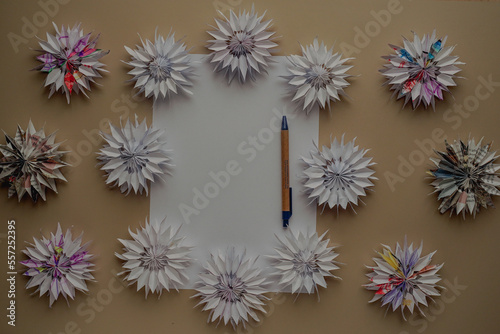 Blank sheet of paper with copy space for text, pen and dimensional paper flowers close-up top view DIY beige background. Place for congratulations or wishes. Christmas decor. Blurred background