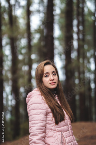 portrait of a woman in the middle of the forest wearing a pink jacket and brown hair