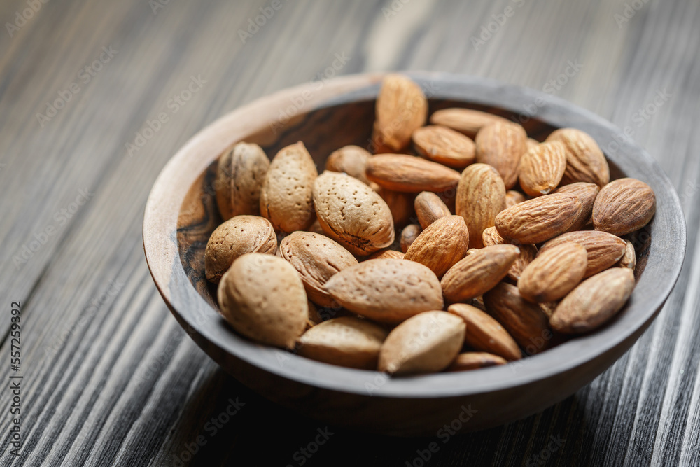 Peeled raw almonds and almonds in a shell in a wooden bowl on a dark wooden background. Peeled raw almonds and almonds in a shell in a wooden bowl on a dark wooden background.