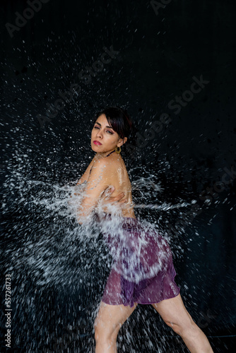 A Lovely Latin Bikini Model Poses In A Studio Environment While Water Is Thrown On Her