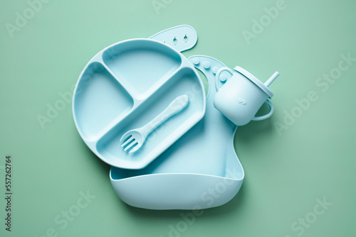 Baby silicone tableware set on color background. Flat lay bowl, plate, fork, baby bip. Top view. photo