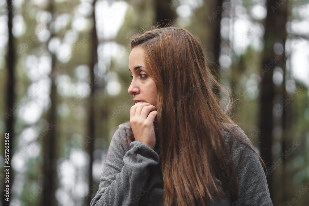 girl with brown hair in the middle of the forest being cold