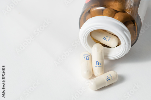 Vitamin B3. Vitamins in capsules. White capsules with vitamin B3, niacinamide or nicotinic acid are scattered on the table from a bottle on a white background. Dietary supplements in tablets. photo