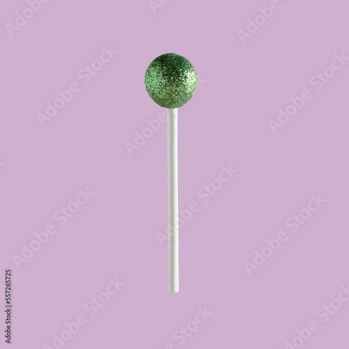 Green Christmas bauble ornament used as a lollipop on lavander pastel background. Minimal design.