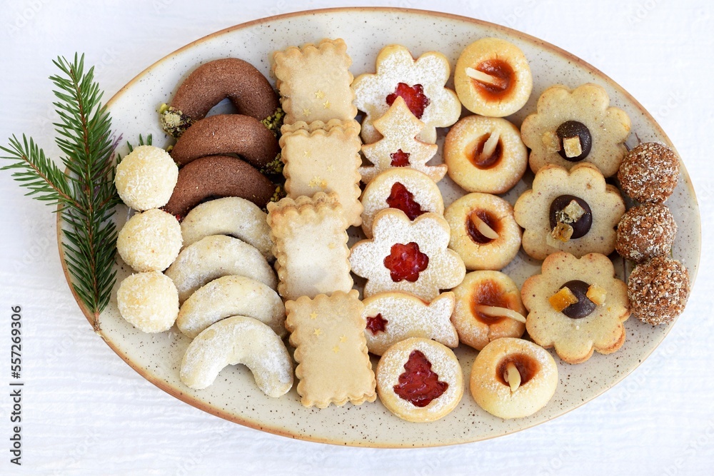 Various kinds of Christmas cookies arranged on a plate, with spruce twig decoration