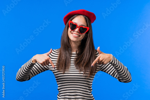 Pretty woman pointing down to advertising area. Blue background. Young lady asking to click to subscribe below. Copy space for your commercial idea, promotional content.