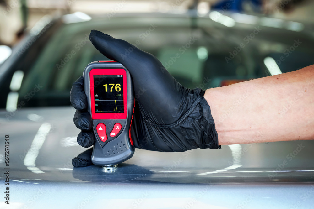 Close-up of a mechanic's hand holding a magnetic thickness gauge. Instrument for measuring paint thickness. Checking a car at a service station Close-up of a mechanic's hand holding a magnetic thickness gauge. Instrument for measuring paint thickness. Checking a car at a service station