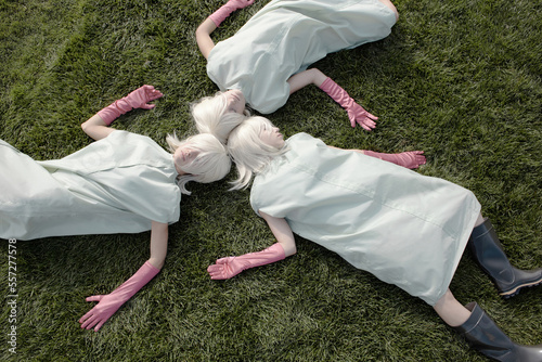 Directly above view of unrecognizable alike women with white blond hair wearing garment covers and pink gloves sleeping on green lawn    photo