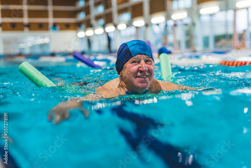 Side view of older adult man swimming with a pool noodle . High quality photo