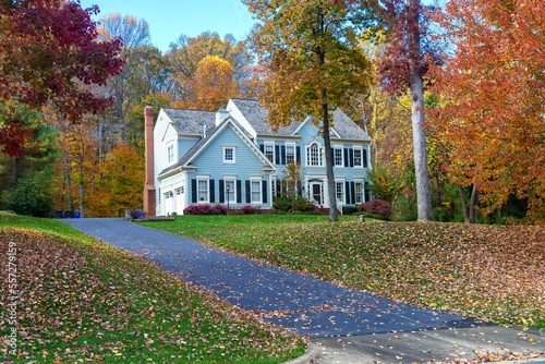 private two-storey house among autumn trees. Asphalt driveway to garage.