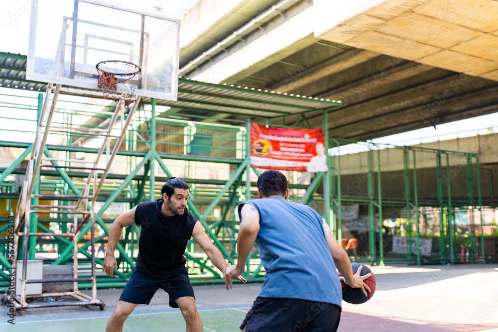 Two man athlete playing streetball match shooting and defense basketball on outdoors court together in sunny day. Sportsman do sport training basketball at street court under highway in the city. Two man athlete playing streetball match shooting and defense basketball on outdoors court together in sunny day. Sportsman do sport training basketball at street court under highway in the city.