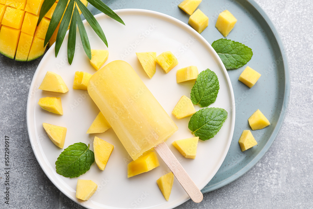 Plate of tasty mango ice pop on grey table, flat lay. Fruit popsicle
