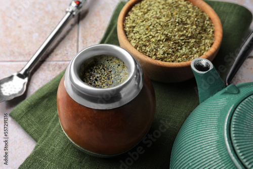 Calabash, bombilla, bowl of mate tea leaves and teapot on tiled table, closeup