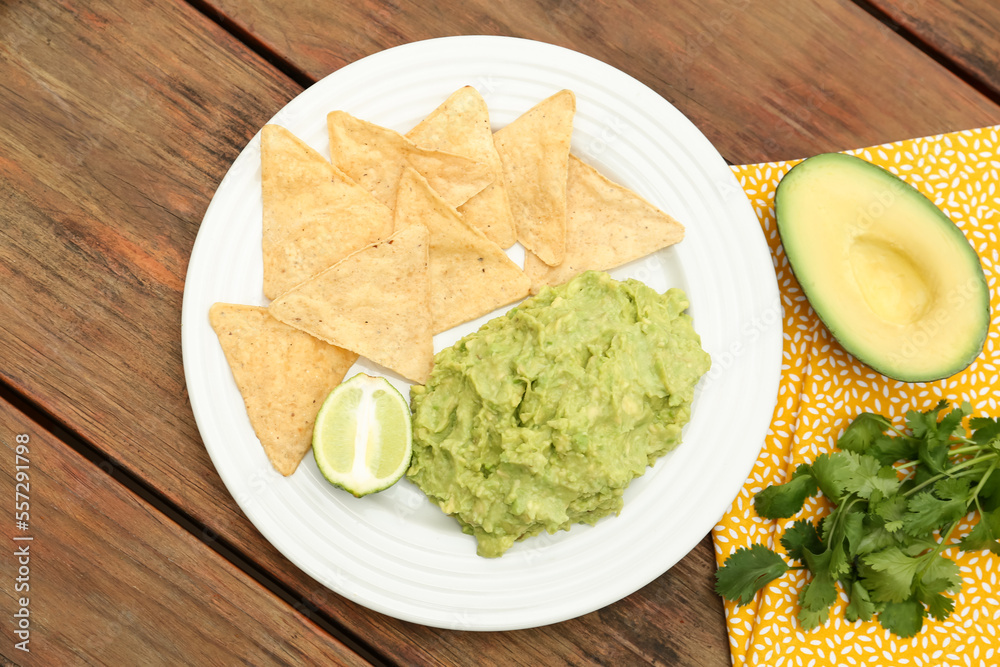Delicious guacamole made of avocados, nachos and lime on wooden table, flat lay Delicious guacamole made of avocados, nachos and lime on wooden table, flat lay