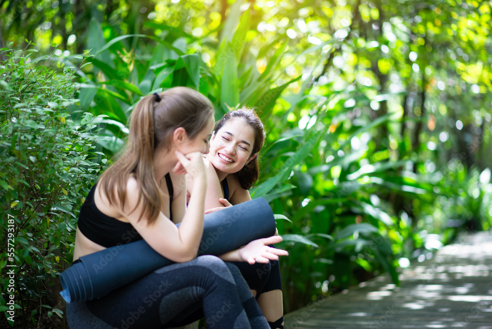 Couple of young sporty women holding yoga mats and talking together at park Couple of young sporty women holding yoga mats and talking together at park
