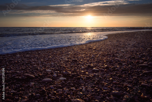 Sonnenuntergang am Meer mit Wellen und kleinen Steinen am Strand