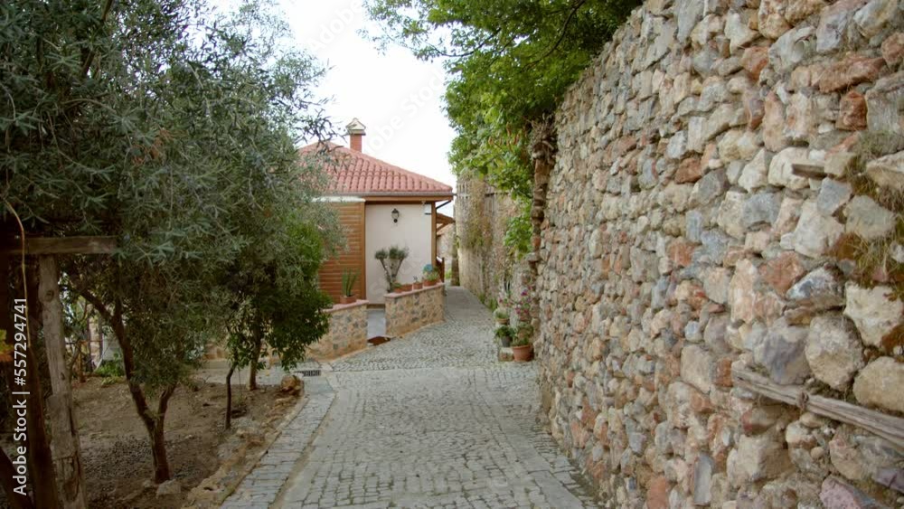 Footpath in old village. stone-paved footpath next to large fence made of old stones with cute little houses visible in distance. Footpath in old village. stone-paved footpath next to large fence made of old stones with cute little houses visible in distance.