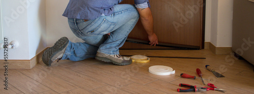 Image of a handyman installing a draft excluder on his front door. Improved thermal insulation and infiltration of cold air. Horizontal banner