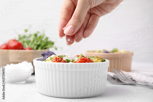 Woman salting delicious salad at white table, closeup