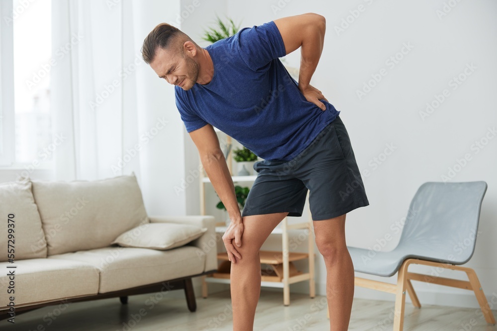 Man backache neck and shoulder pain, inflammation of muscles and ligaments rupture during sports, inflammation and injury, in a blue t-shirt at home Man backache neck and shoulder pain, inflammation of muscles and ligaments rupture during sports, inflammation and injury, in a blue t-shirt at home