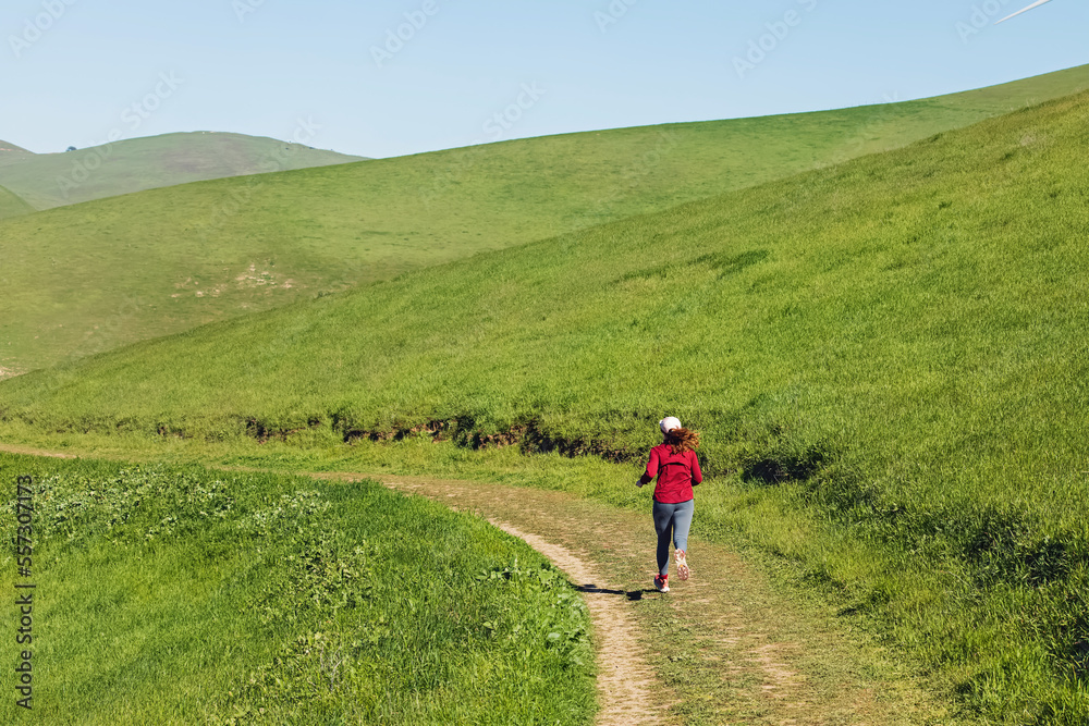 Woman running among the hills covered with green grass