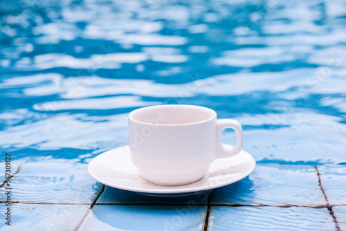 White cup of coffee by the edge of the pool, turquoise water background © ประพันธ์ บุญเหมาะ