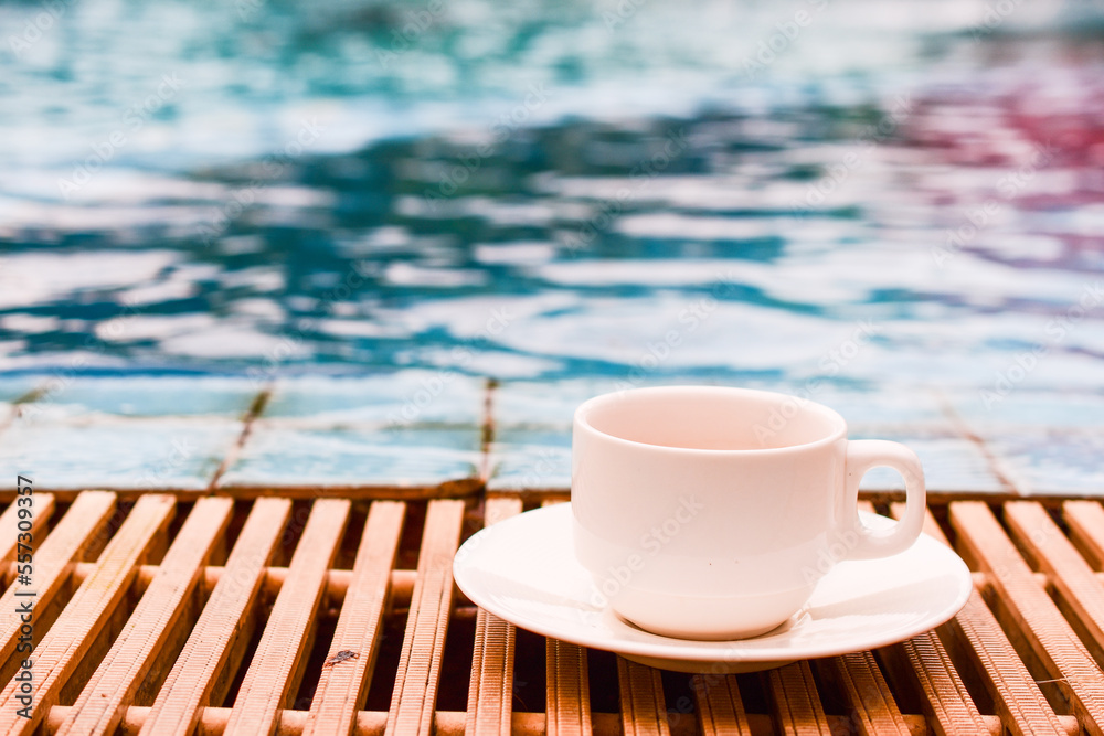 White cup of coffee by the edge of the pool, blurred blue water background White cup of coffee by the edge of the pool, blurred blue water background