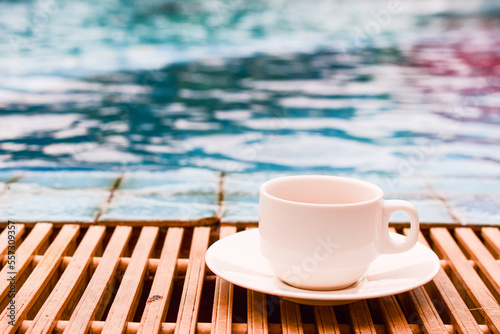 White cup of coffee by the edge of the pool, blurred blue water background