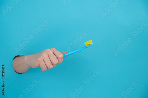 A woman s hand sticks out of a blue paper background and holds a toothbrush. 