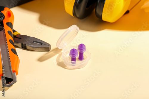 Plastic container with earplugs, pliers and knife on color background