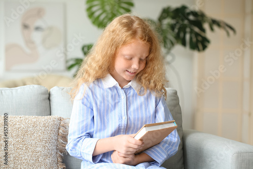 Little girl with old book sitting on sofa at home photo