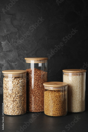 Glass jars with different cereals on dark background