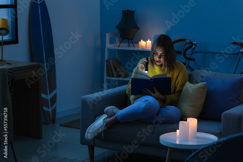 Young woman reading book with flashlight at home during blackout