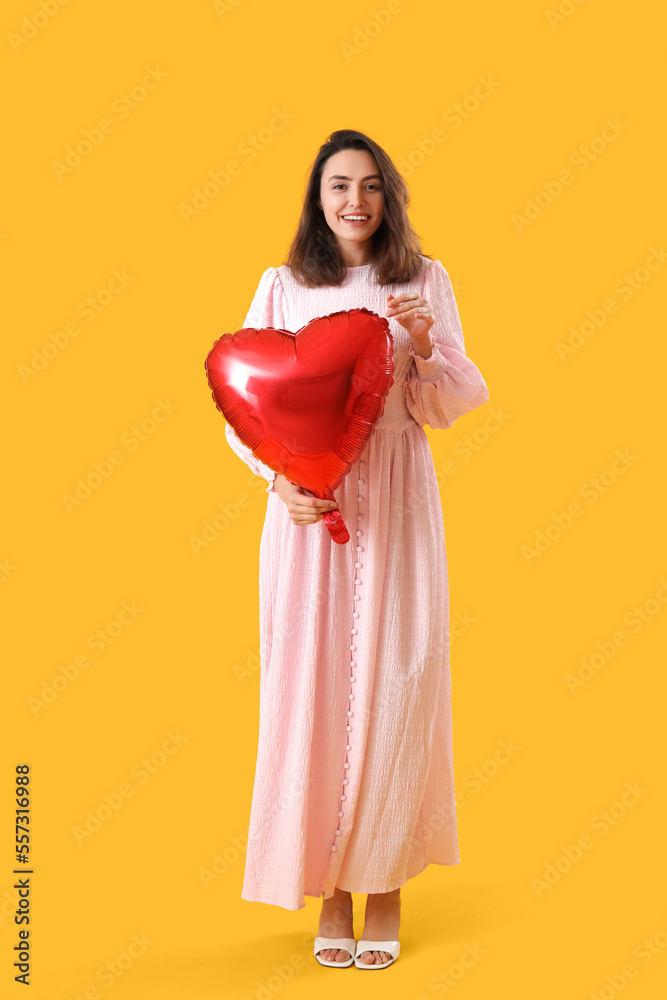 Young woman with heart shaped balloon on yellow background. Valentine's Day celebration Young woman with heart shaped balloon on yellow background. Valentine's Day celebration
