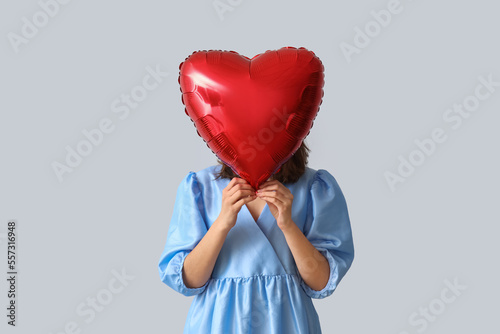 Young woman with heart shaped balloon on grey background. Valentine's Day celebration