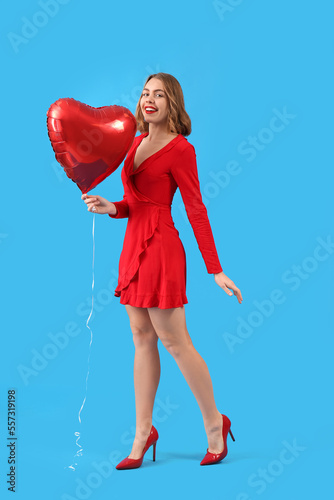 Beautiful young woman with red heart-shaped balloon on blue background