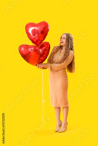 Beautiful young woman with heart-shaped balloons on yellow background. Valentine's Day celebration