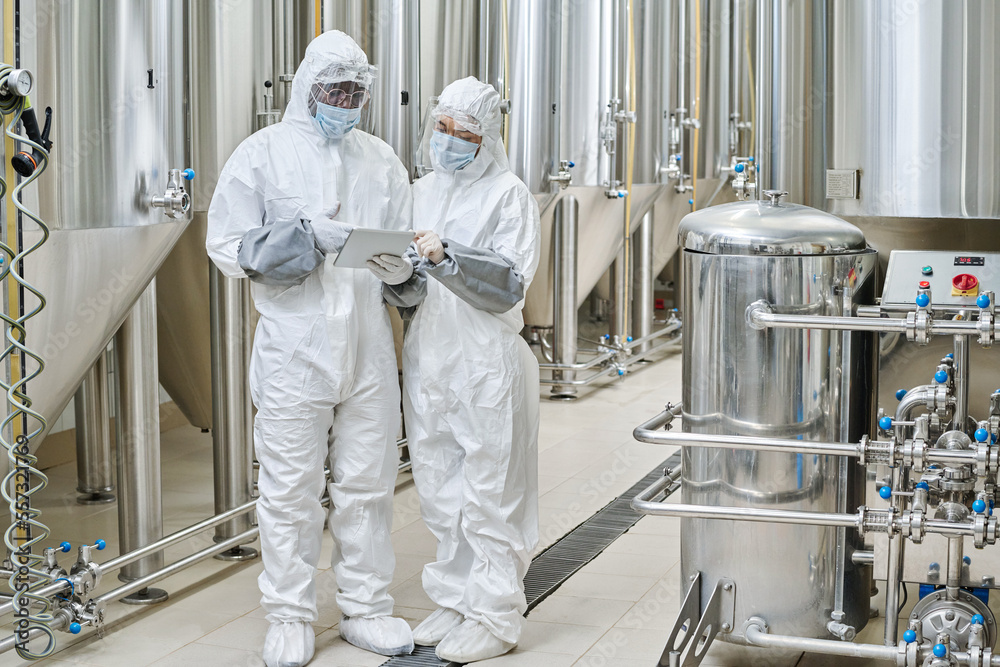 Chemists in protective workwear using tablet pc during their teamwork at chemical factory Chemists in protective workwear using tablet pc during their teamwork at chemical factory