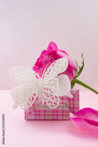 Fototapeta Naklejka Na Ścianę i Meble -  Gift box with shiny butterfly, rose and petal on pink background. Birthday, March 8, Valentine's, International Women's Day. Copy space