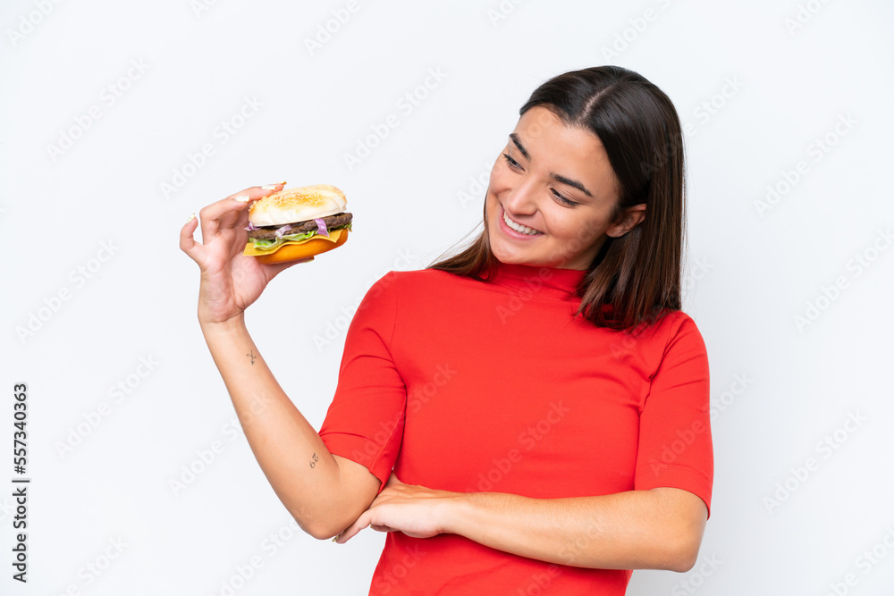 Young caucasian woman holding a burger isolated on white background with happy expression Young caucasian woman holding a burger isolated on white background with happy expression