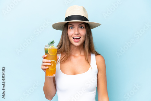 Young beautiful woman holding a cocktail isolated on blue background with surprise and shocked facial expression