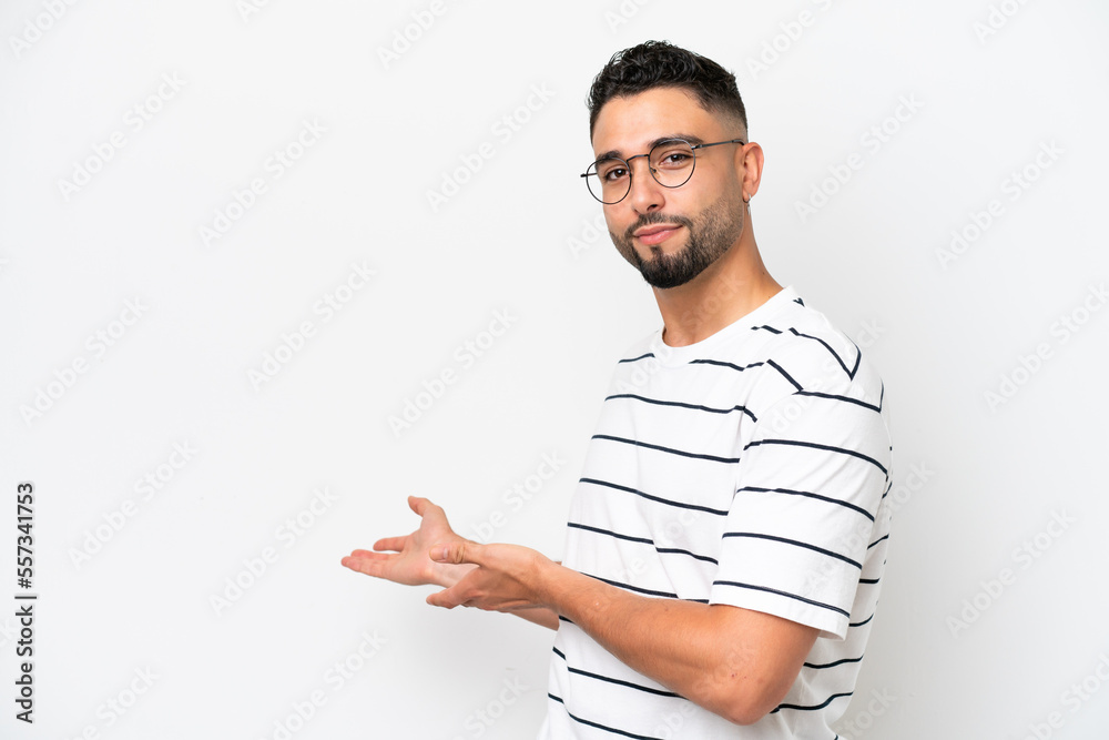 Young Arab handsome man isolated on white background extending hands to the side for inviting to come Young Arab handsome man isolated on white background extending hands to the side for inviting to come