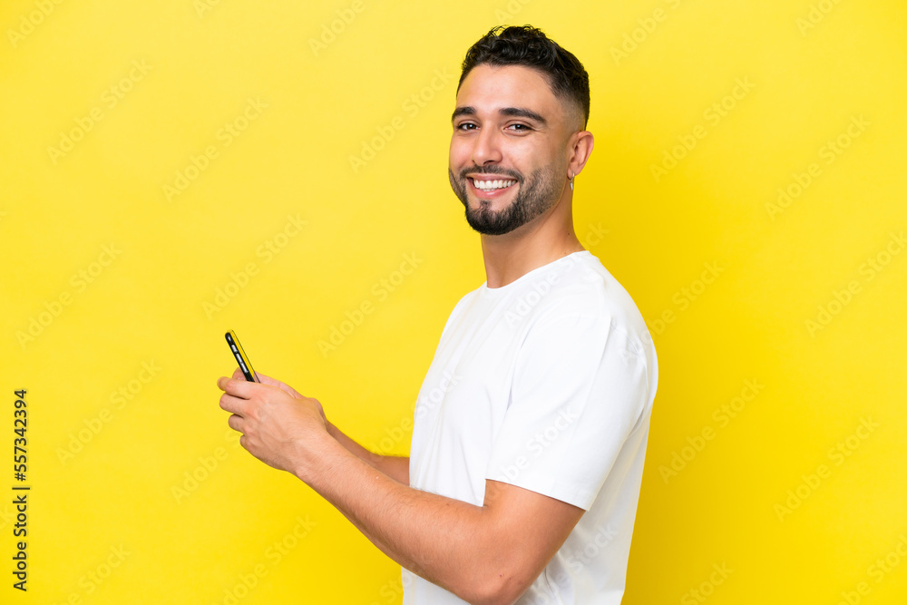 Young Arab handsome man isolated on yellow background sending a message or email with the mobile Young Arab handsome man isolated on yellow background sending a message or email with the mobile