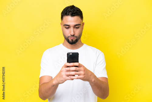 Young Arab handsome man isolated on yellow background using mobile phone