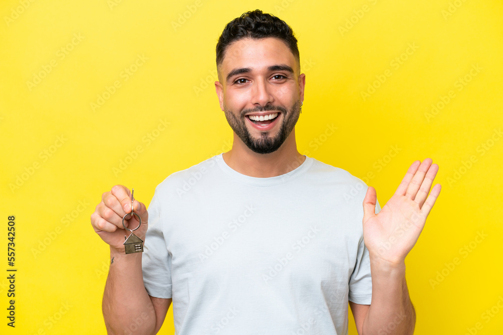 Young Arab man holding home keys isolated on yellow background with shocked facial expression Young Arab man holding home keys isolated on yellow background with shocked facial expression