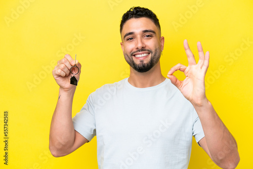 Vászonkép Young Arab man holding home keys isolated on yellow background showing ok sign w