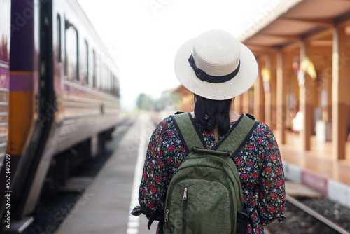 Back view of woman traveller at railway station, wear white hat and backpack. Concept, travel by train in Thailand . Transportation. Alone journey. Weeken, holiday or vacation trip. 