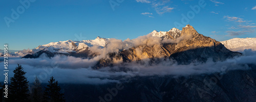 image panoramique avec une vue magnifique sur les montagnes enneigées des Alpes. le soleil éclaire le sommet des montagnes avec un beau ciel bleu et quelques nuages.